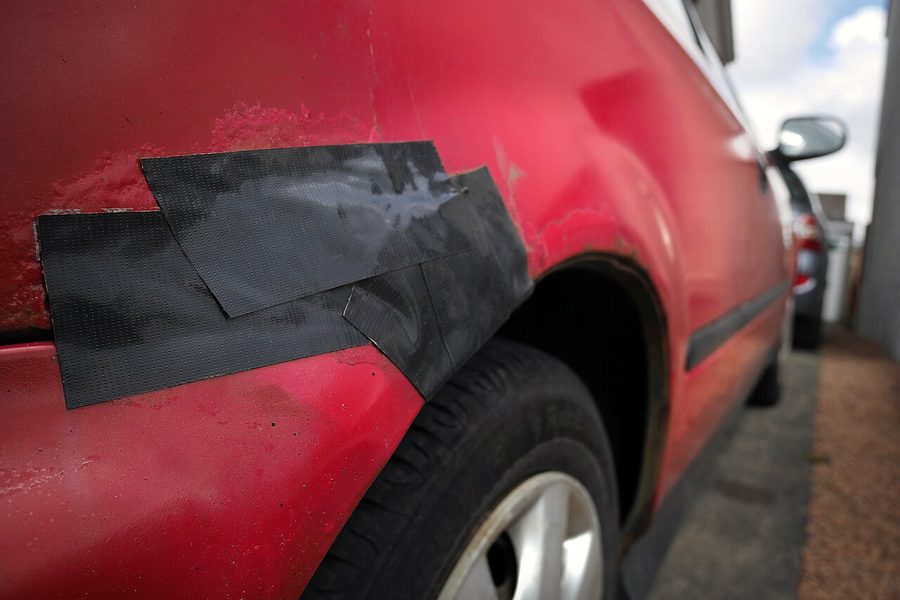 Rode auto waarvan een roestplek met tape is afgeplakt